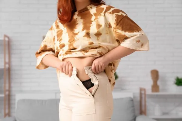 Image of woman trying to do her trousers up after pregnancy weight gain Chipping Norton